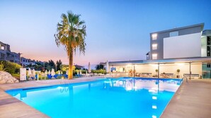 A swimming pool with lounge chairs and umbrellas, surrounded by modern buildings and a palm tree.