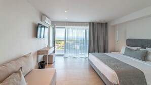 A modern hotel room with a large bed, a sofa, a desk, and a balcony with a view.