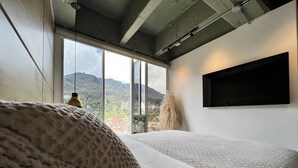 A bedroom with a large window, a bed, and a mounted TV.