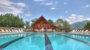 A swimming pool with lounge chairs and a wooden pavilion in the background. - NEW! Western Cabin, Super Fast Free WiFi, NFL Sunday, Arcade, Fishing & 2 Pools! (Sevierville)