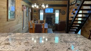 A wooden cabin interior with a stone countertop, a fireplace, a television, and a staircase. - NEW! Western Cabin, Super Fast Free WiFi, NFL Sunday, Arcade, Fishing & 2 Pools! (Sevierville)