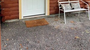 A wooden cabin with a white door, a bench with cushions, and a small window. - Shawnee Tiny Cabin near Ferne Clyffe with Hot Tub (Goreville)