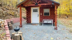 A small wooden cabin with a white door, a bench outside, and a number '4' sign. - Shawnee Tiny Cabin near Ferne Clyffe with Hot Tub (Goreville)
