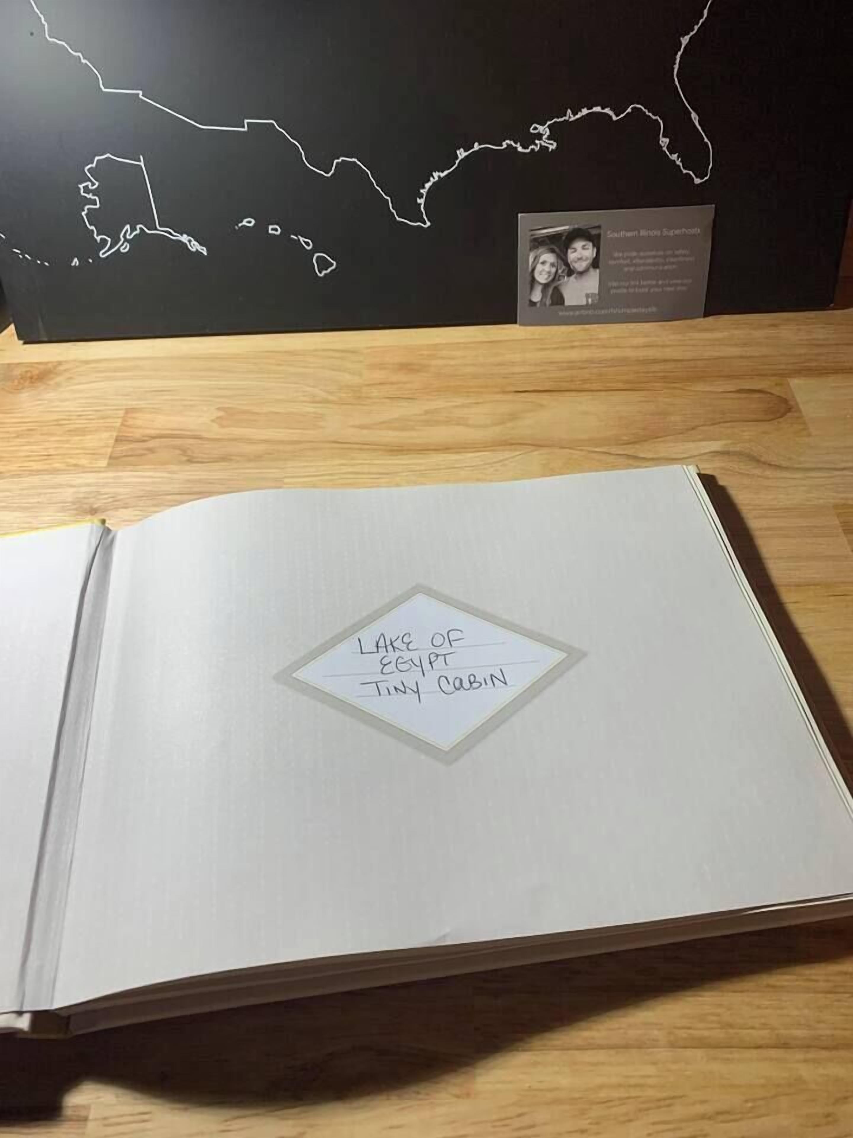 An open book with a handwritten note on the page that reads "Lake of Egypt Tiny Cabin."