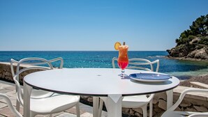 Une table ronde avec un verre, des chaises blanches et une vue sur la mer.