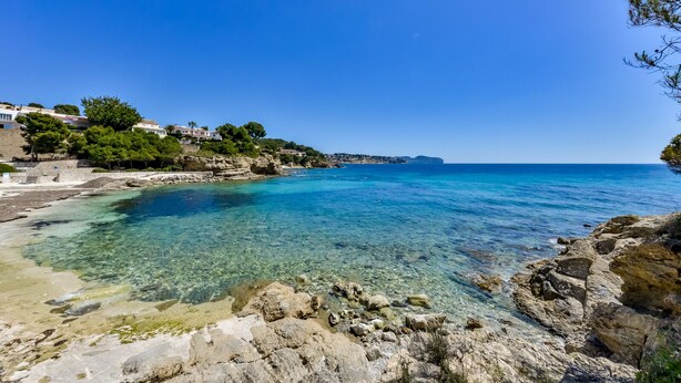 Un paysage côtier avec une eau bleue et limpide, des rivages rocheux et des bâtiments situés sur une colline.