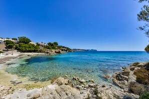 A coastal scene with clear blue waters, rocky shorelines, and buildings on a hillside.