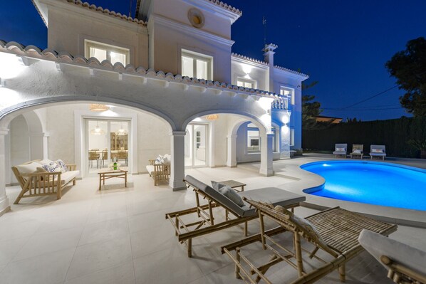 A modern house with a swimming pool, outdoor seating, and a well-lit patio area.