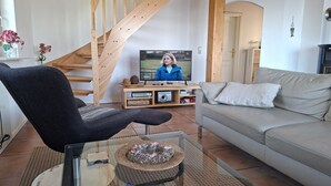 A living room with a sofa, a chair, a TV, a wooden staircase, and a door. - View of the lake - vacation home with a fantastic view (Sternberg)