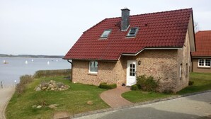 A brick house with a red roof, a small porch, and a view of a lake with sailboats. - View of the lake - vacation home with a fantastic view (Sternberg)