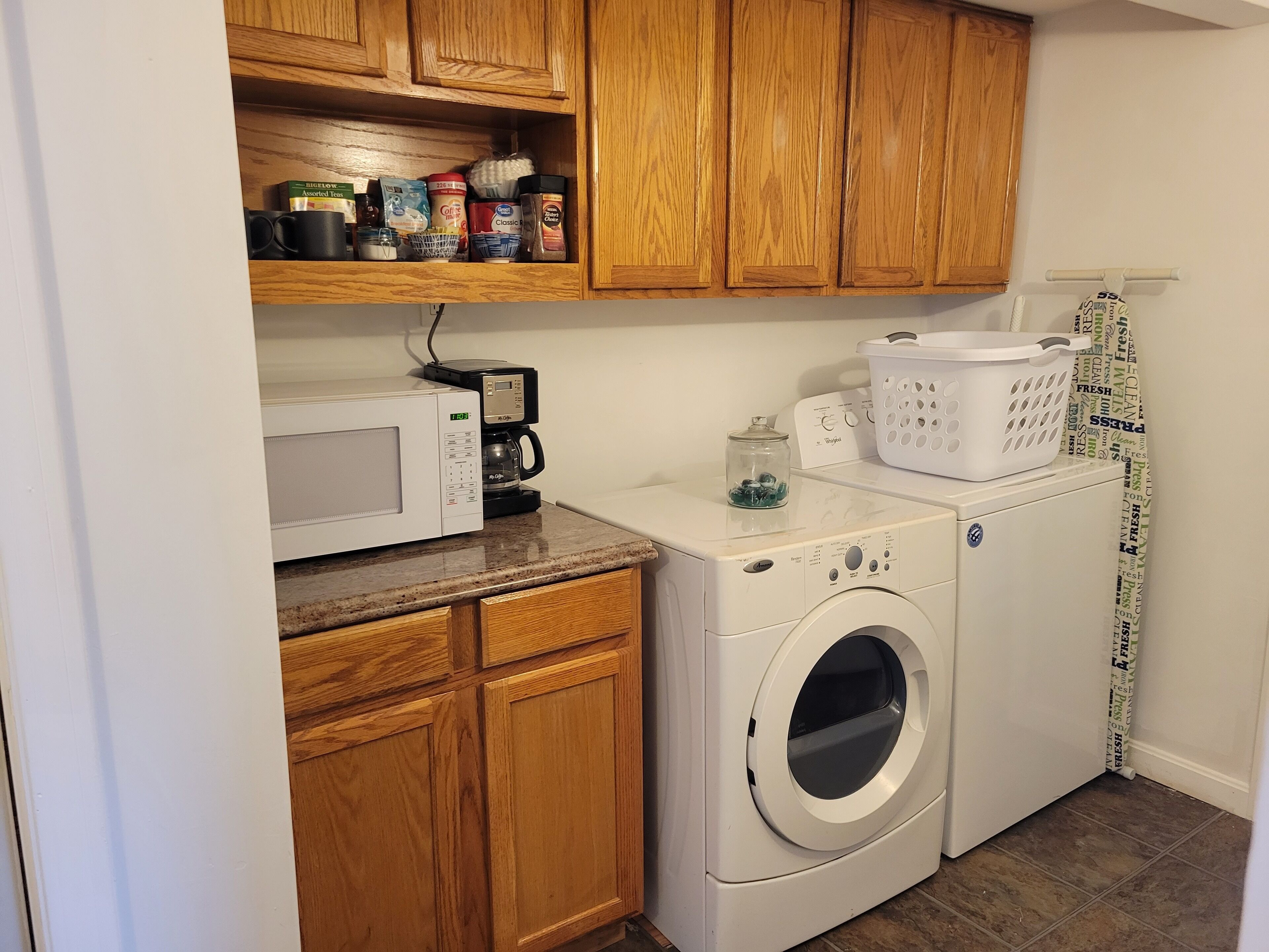 A compact laundry area with a washing machine, a coffee maker, and a microwave on the countertop.