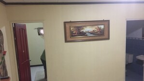 A hallway with a door leading to a room, a framed painting on the wall, and a tiled floor.