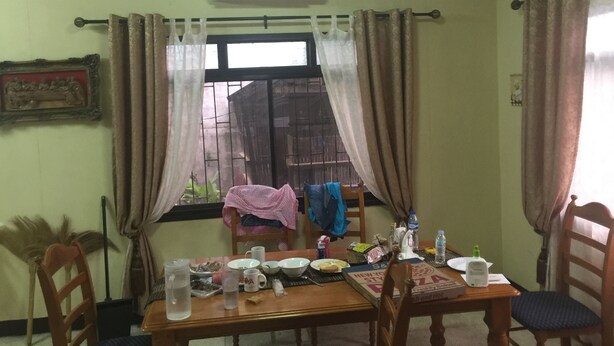 A dining area with a table set for two, a window with curtains, an air conditioning unit, and a framed picture on the wall.
