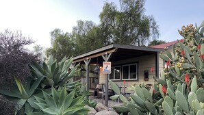 A rustic guesthouse with a covered patio, surrounded by large cacti and agave plants. - PCH Bunkhouse (San Luis Obispo)