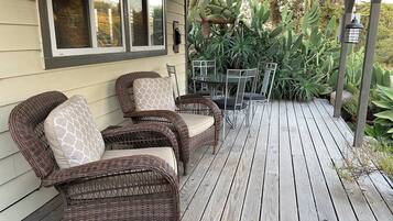A covered porch with wicker furniture and a table, surrounded by various plants.