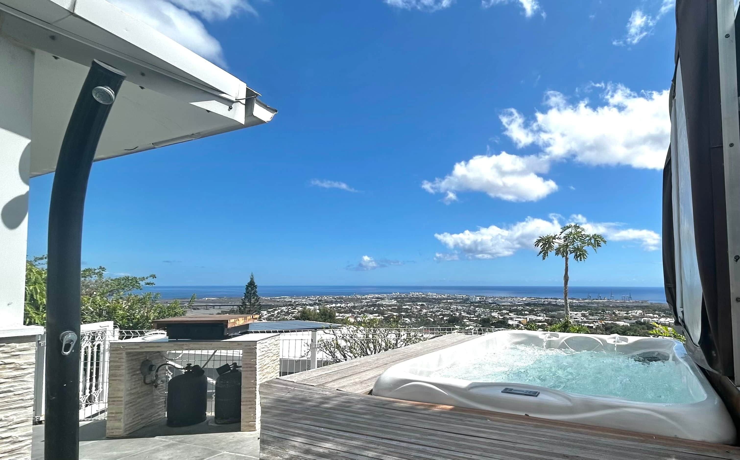 Ein Whirlpool auf einer Holzterrasse mit freiem Blick auf das Meer und eine Stadtlandschaft im Hintergrund.
