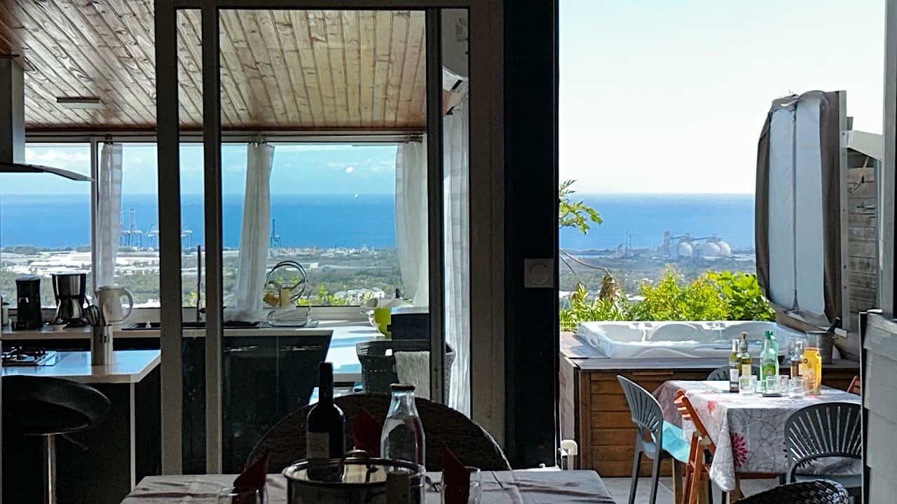 Un coin repas avec vue sur l’océan, une table dressée avec des verres et des bouteilles, et un téléviseur fixé au mur.