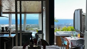 A dining area with a view of the ocean, a table set with glasses and bottles, and a television on the wall.