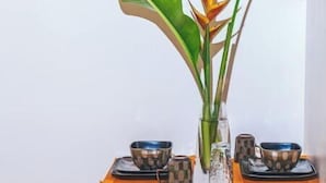 A dining area with a white table, two stools, and a plant with large leaves and a yellow flower.