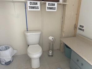 Et badeværelse med toilet, skraldespand og skilte, der angiver områder til 'CLEAN TOWELS' og 'USED TOWELS'.