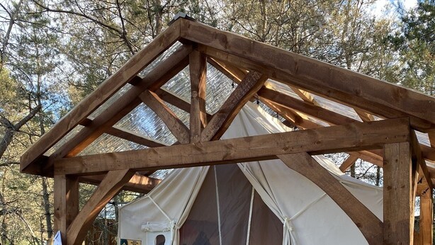 Ein hölzerner Pavillon mit überdachtem Eingang, zwei Kübelpflanzen und einer Bank.