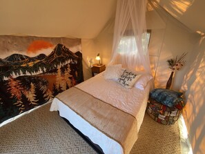 Et soveværelse med en seng, et sengebord med en lampe, et vægtæppe på væggen og en dekorativ vase.
