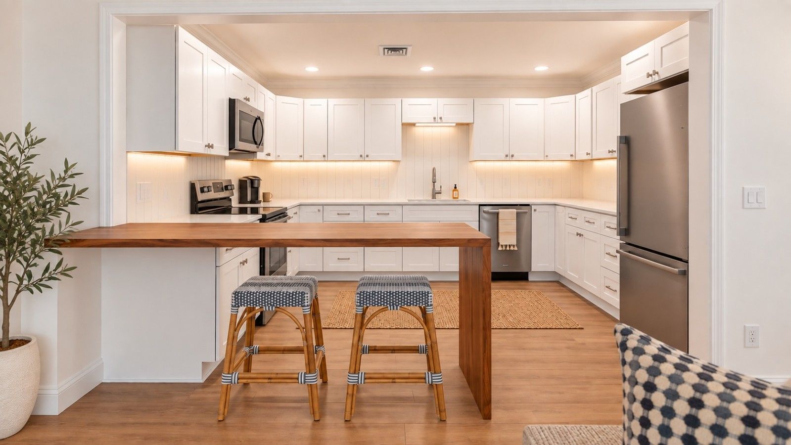 Een moderne keuken met witte kasten, een houten keukeneiland, twee barkrukken en een inbouwmagnetron.