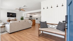 Una sala de estar moderna con un sofá, un banco de madera, un televisor y un ventilador de techo.
