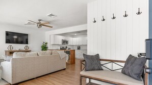 A modern living room with a sofa, a bench, a TV, and a kitchen in the background.