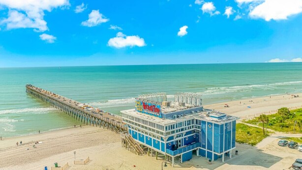 A pier extending into the ocean with a building adjacent to the beach.