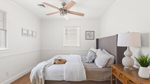 A bedroom with a bed, a ceiling fan, a bedside table with a lamp, and a window with blinds.