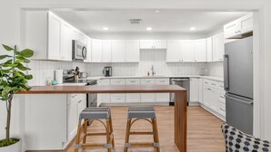 A modern kitchen with white cabinets, a wooden island, two bar stools, and a large refrigerator.