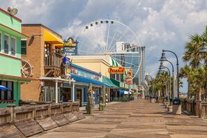 Une promenade en bord de mer bordée de boutiques, une grande roue et un bâtiment moderne en arrière-plan.