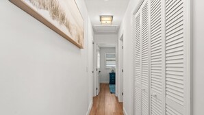 A hallway with white walls, wooden flooring, and white closets with louvered doors.