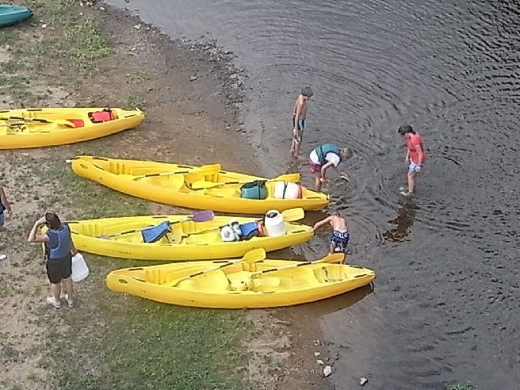 A group of people near yellow kayaks on a sandy shore.
