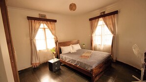 Una camera da letto con un letto in legno, un comodino, un tavolino con un vaso e una ventola da terra.