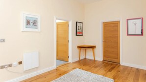 A hallway with wooden flooring, a radiator, and three framed pictures on the walls. - Stylish 2 Bedroom Apartment in Greenwich (London)