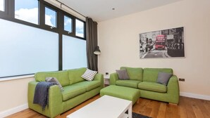 A living room with two green sofas, a white coffee table, and a black-and-white city street painting on the wall. - Stylish 2 Bedroom Apartment in Greenwich (London)
