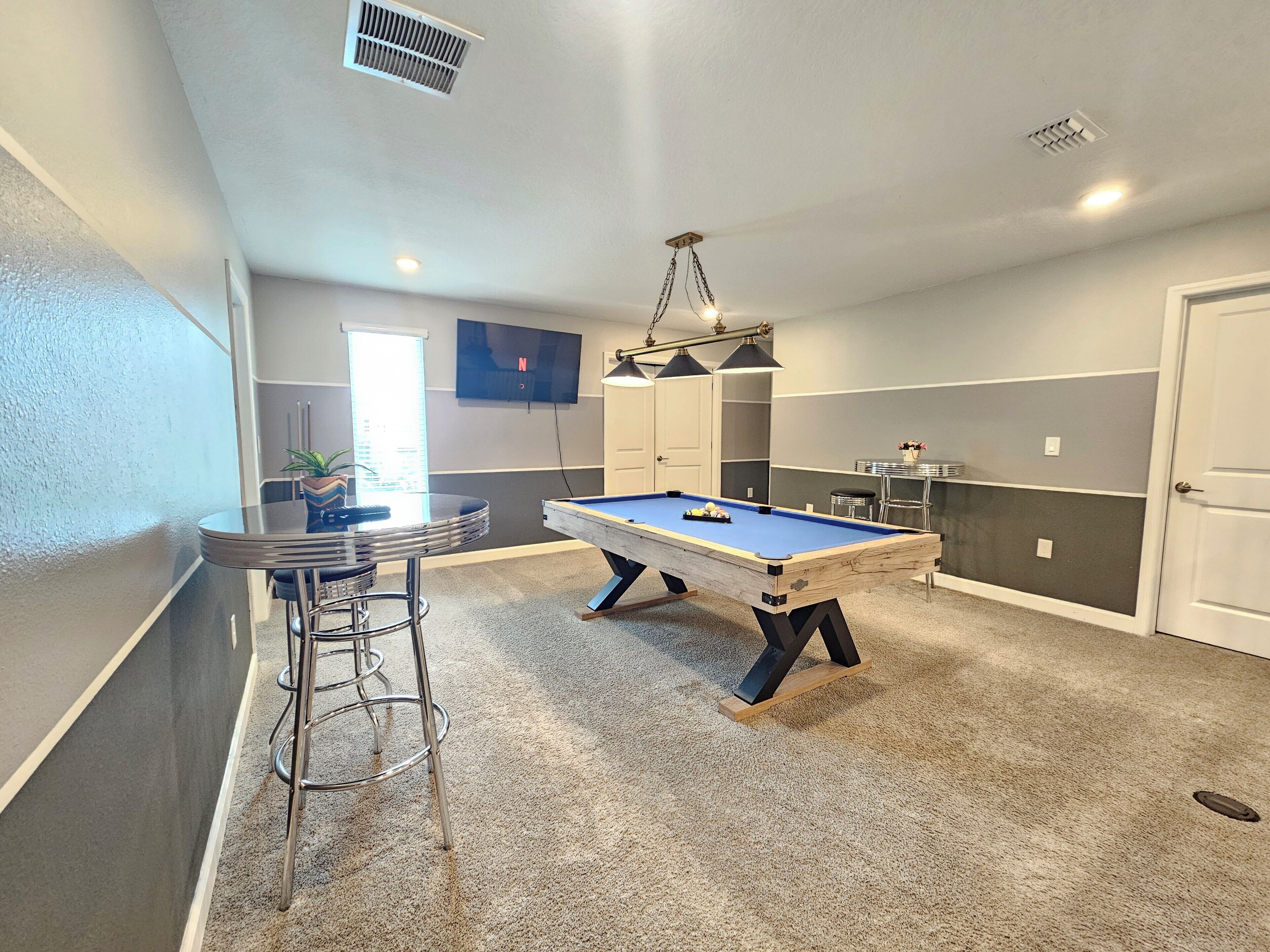 Une table de billard dans une pièce qui comprend un bar, des chaises et un téléviseur fixé au mur.