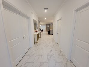 Un pasillo con puertas blancas, suelo de mármol y un comedor con mesa y sillas.