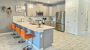 A modern kitchen with a central island, stainless steel appliances, and a bar seating area. - Disney theme park 10 mmins/Storey Lake 9 Beds /Lake View Single House (kissimmee)