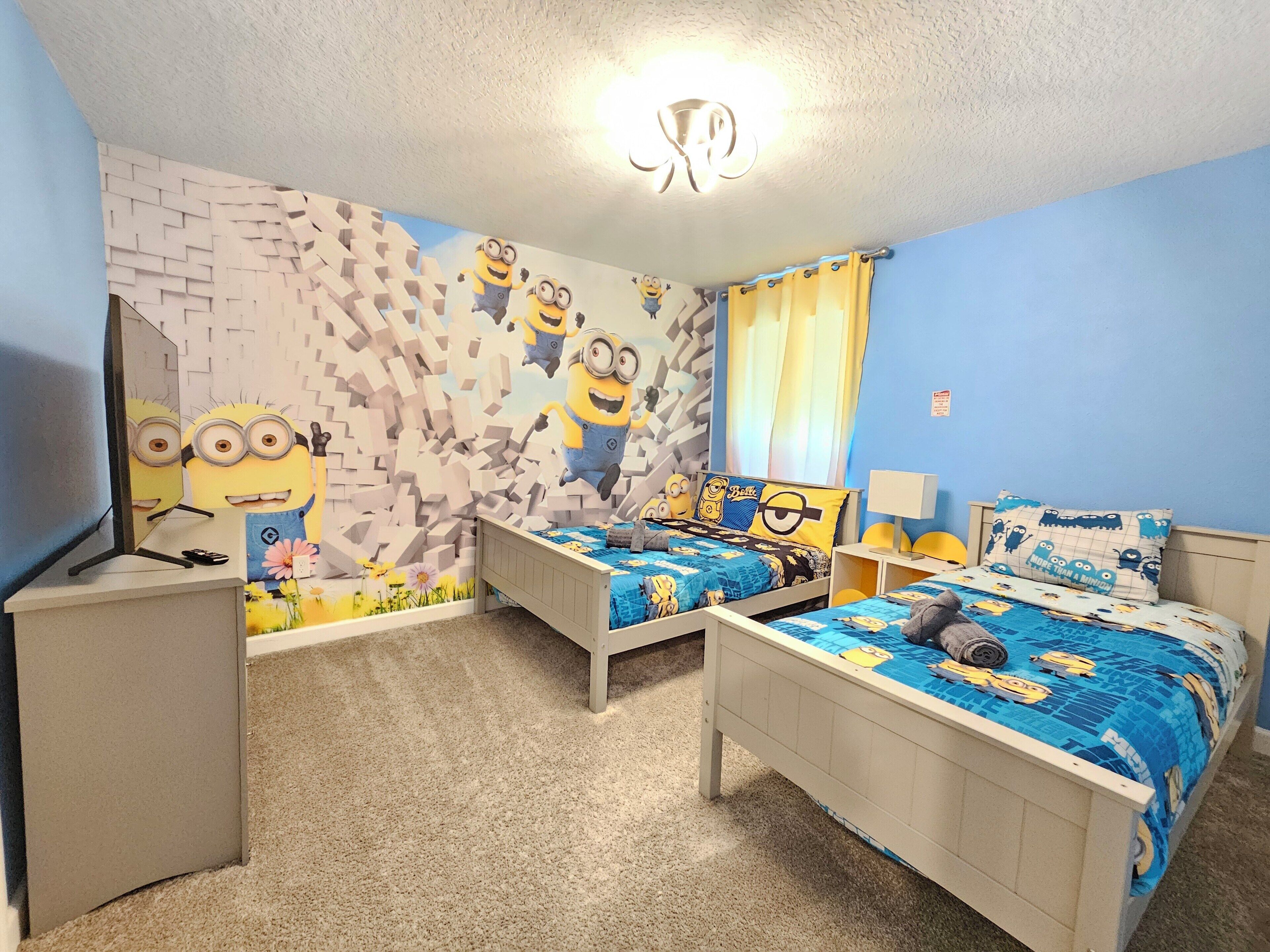 Ett sovrum med två sängar, en tv och en väggmålning med motiv av Minions.