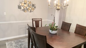 Une salle à manger avec une table en bois, des chaises, un lustre et une œuvre d’art murale.