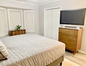 Une chambre à coucher avec un lit, une commode, un téléviseur et un placard.