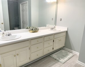 Une salle de bain avec un meuble-lavabo blanc, deux vasques, un grand miroir et un petit tapis.