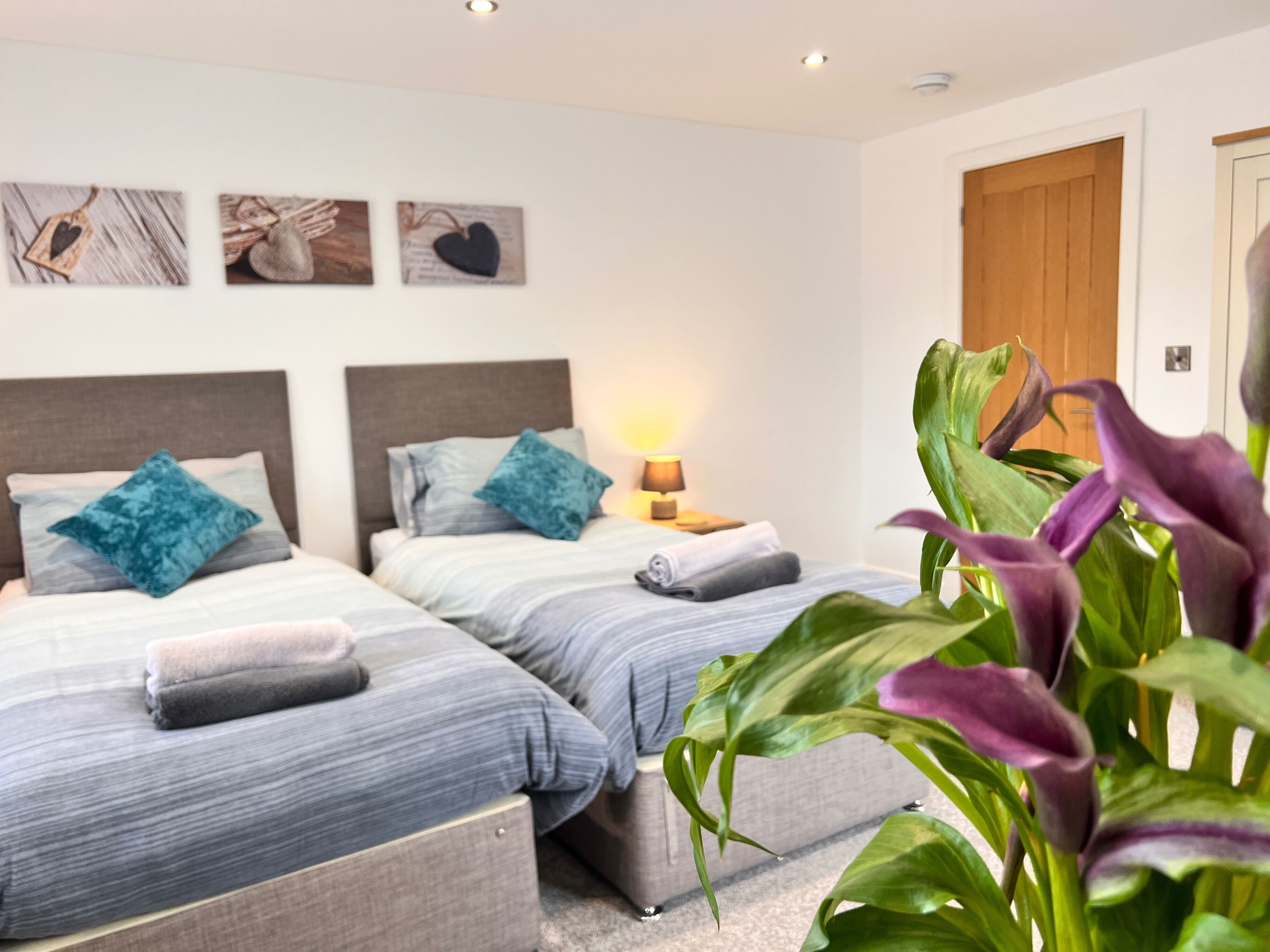 A hotel room with two beds, a nightstand with a lamp, and a large plant.