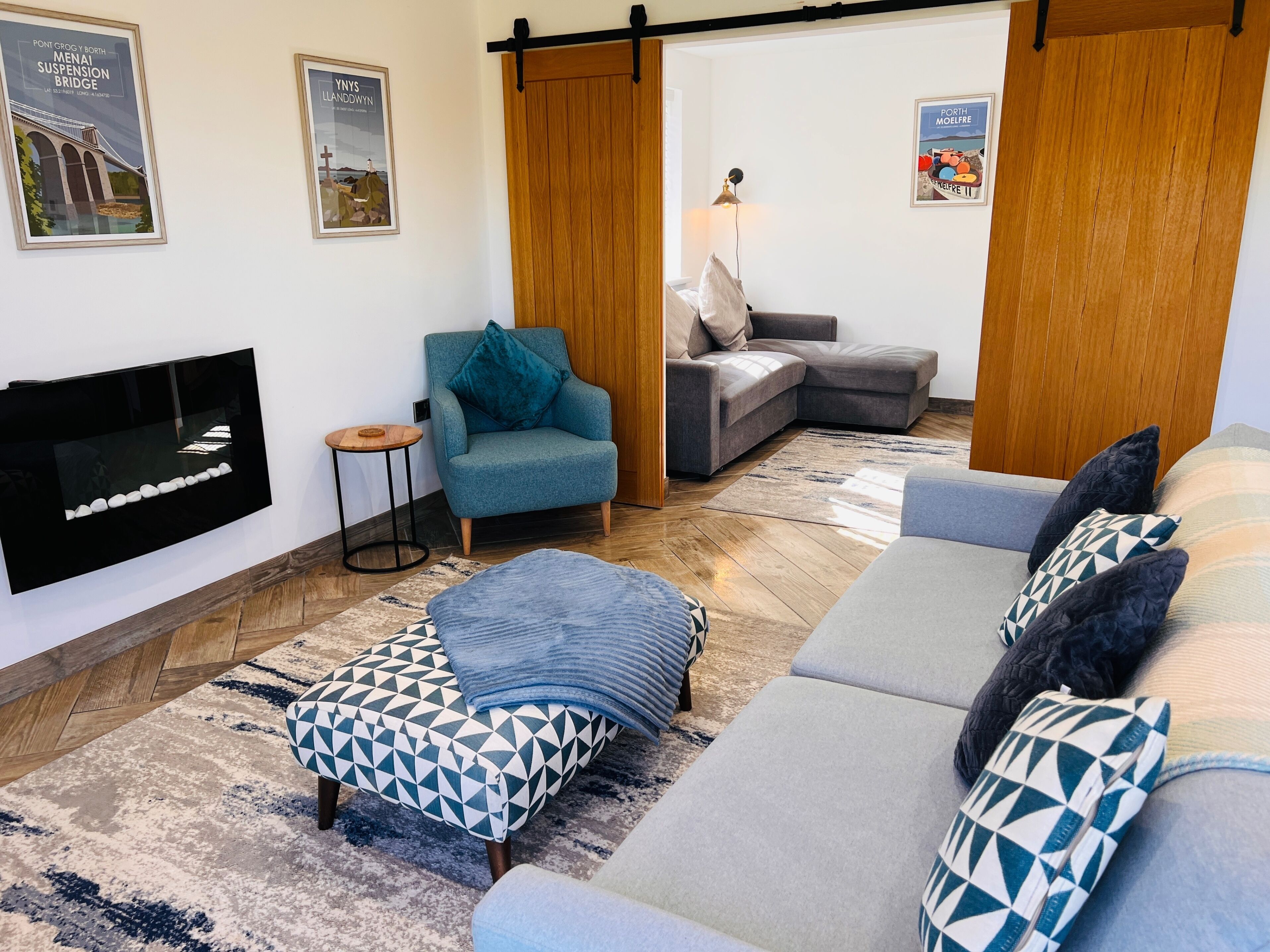 Una sala de estar moderna con un televisor de pantalla plana, un sillón color turquesa, un sofá gris y un reposapiés estampado.