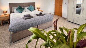 A bedroom with a bed, bedside tables, a wardrobe, and ceiling lights. - Stylish, Dog Friendly Coastal Bungalow With Garden (Holyhead)