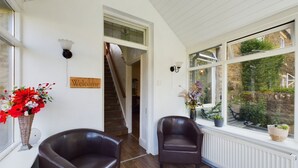 A cozy room with a wooden floor, two leather chairs, a 'Welcome' sign, a staircase, and a window with a view of greenery. - Acacia House  - Holiday Cottage Wolsingham (Wolsingham)