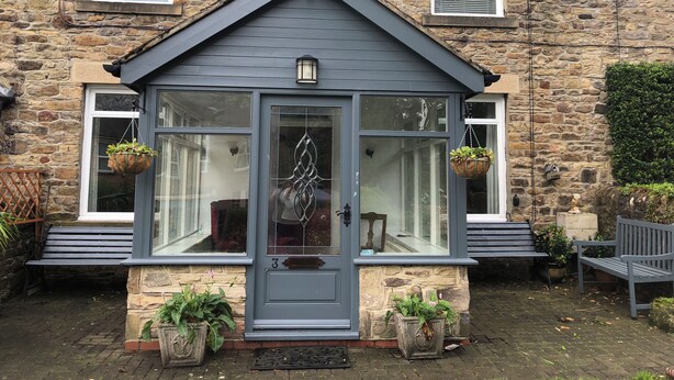 A stone house with a grey front door, two hanging flower baskets, and a bench outside. - Acacia House  - Holiday Cottage Wolsingham (Wolsingham)